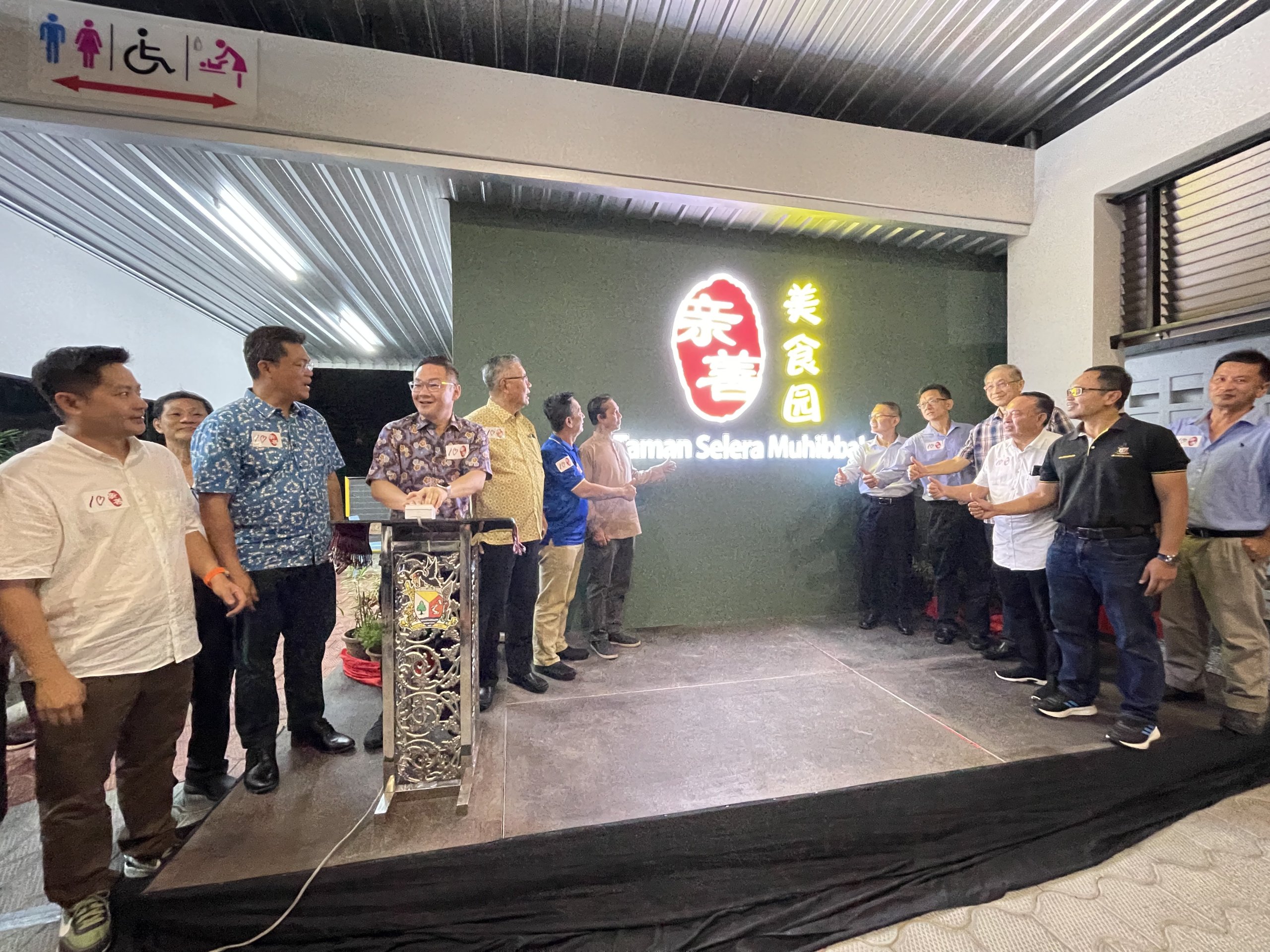 Tiang (third left) switches on the lights of the Taman Selera Muhibbah signboard to officially open the food court while (from fourth left) Ting, Yong and Bujang look on.