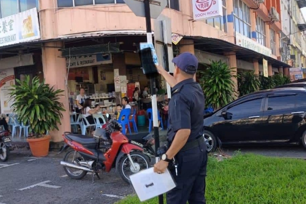 An enforcement personnel taking down an advertising poster pasted on the pole of a traffic signboard at one of Sibu’s commercial areas. — Photo via Facebook / Mohammed Abdullah Izkandar Roseley