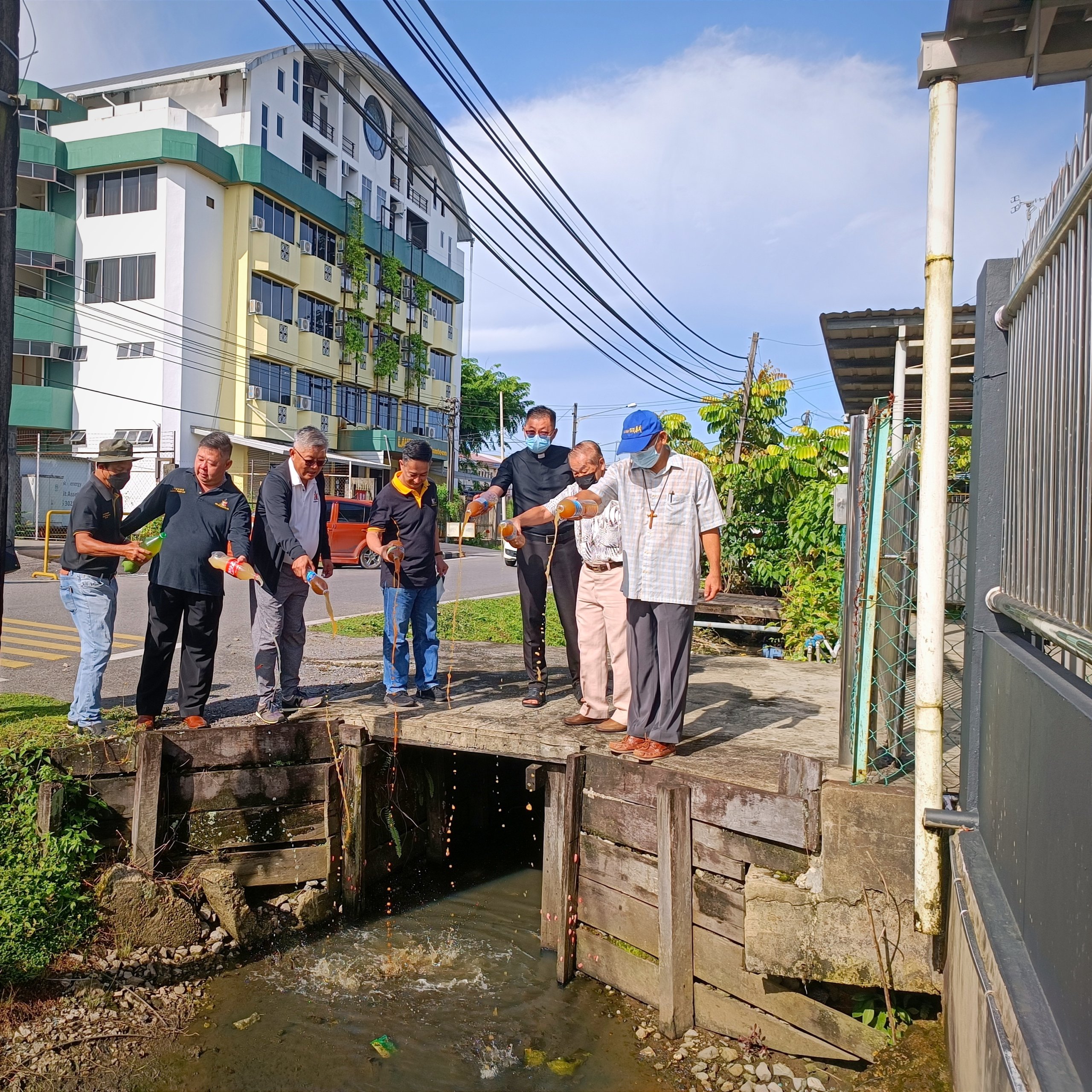 Ting (third left), Bujang (left) and others pouring enzymes into the drains at Jalan Bukit Assek. – Photo by Peter Boon